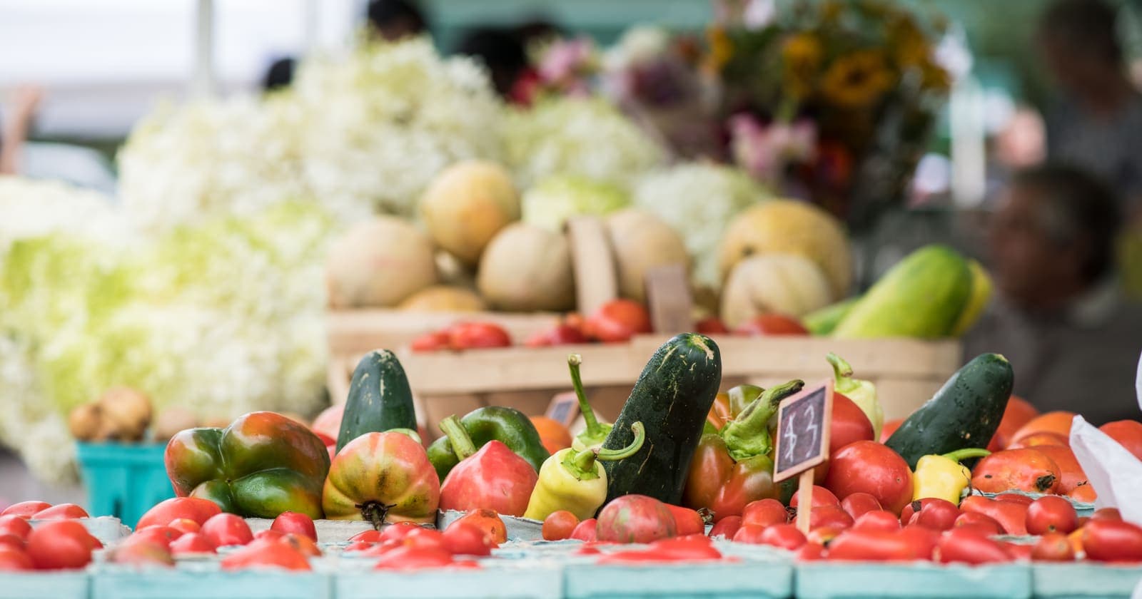 Pint boxes of tomatoes, peppers and cucumbers on a stall at the USDA Farmers Market in Washington, D.C., with melons and cut flowers behind